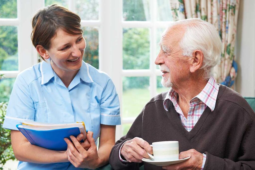 An older adult sitting comfortably in a communal living area, chatting with another resident over coffee.