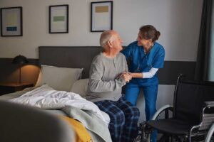 Caregiver assisting an older resident with hand hygiene in a clean assisted living common area.